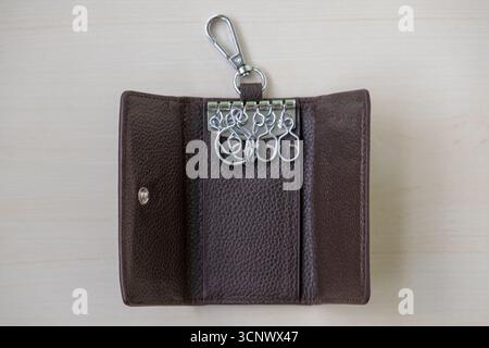 Geöffneter Schlüsselhalter aus Leder auf hellbraunem, strukturiertem Hintergrund. Ledertasche zur Aufbewahrung von Schlüsseln, Innenansicht. Stockfoto