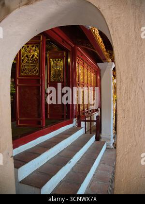 Goldene Türen und rote Wände im Tempel - Ein niedriger Blick auf einen Tempelbogen, der rote und goldene dekorative Wände und Stufen umrahmt, führt zu einem traditionellen Stockfoto