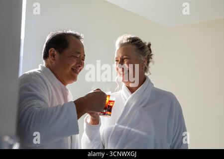 Verschiedene Seniorenpaare tragen Bademäntel, die sich in einem sanft beleuchteten Raum mit Glasbechern gegenüberliegen Stockfoto