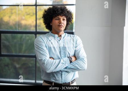 Mann, der Arme gekreuzt hat, trägt blaues Hemd, Armbanduhr, Gürtel im Studio um Fenster Stockfoto