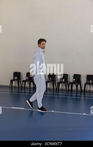 Ein Mann in 20 Jahren, der auf einem polierten blauen Sportplatz läuft, in grauem Trainingsanzug und Schuhen Stockfoto