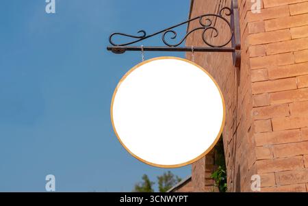 Weißes, leeres rundes Schild, das an einem orangen Gebäude mit blauem Himmel hängt. Sapce kopieren. Stockfoto