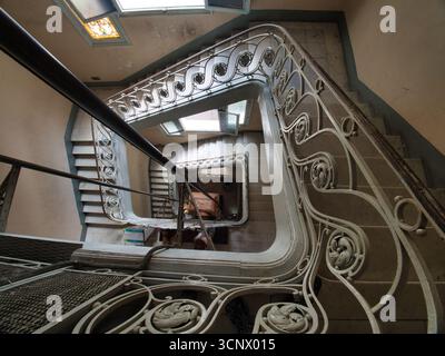Historische Jugendstiltreppe im Gebäude - Eine Hochwinkelaufnahme einer wunderschönen, alten Wendeltreppe mit komplizierten schmiedeeisernen Geländern und klassischem Stil Stockfoto