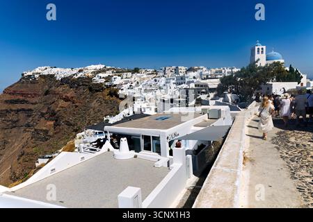 Ein malerischer Blick auf das Dorf Oia in Santorin, Griechenland, mit seiner berühmten weiß getünchten Architektur und einer blau gewölbten Kirche vor einem klaren blauen Himmel Stockfoto