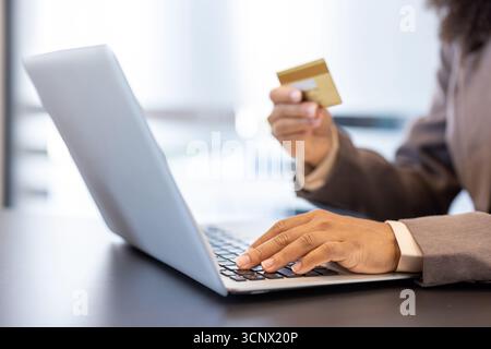 Nahaufnahme eines Körperteils, weibliche Hände einer schwarzen Frau in einem Anzug, die an einem Laptop arbeitet und eine Kreditkarte hält. Stockfoto