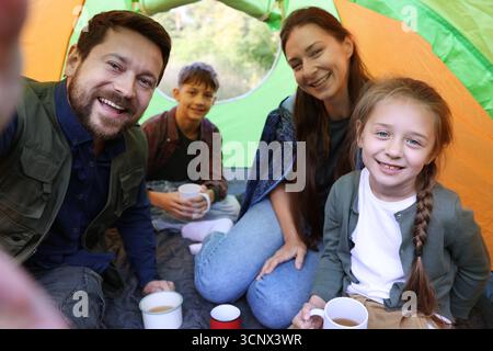 Glückliche Familie, die Selfie im Campingzelt macht, mit Tassen mit heißem Getränk draußen Stockfoto
