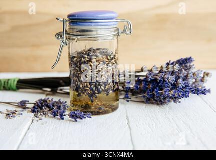 Hausgemachtes, kalt infundiertes Lavendelöl. Olivenöl bedeckt getrocknete Lavendelblüten in einem Glas mit Lavendelstrauß. Stockfoto
