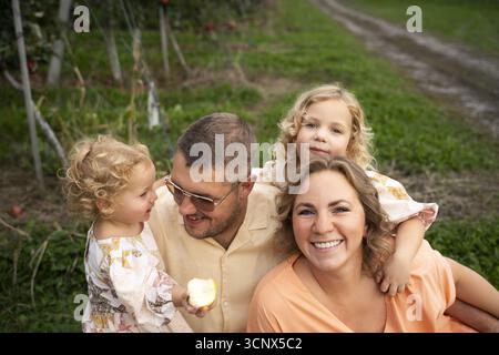 Glückliche Familie, die sich in einem Apfelgarten umschließt und lächelt. Die Szene fängt die Wärme der Familienliebe und die Schönheit der Natur ein, während die Kinder es genießen Stockfoto