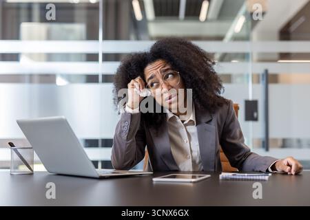Müde afroamerikanische junge Frau, die sich am Arbeitsplatz im Büro unwohl fühlt. Stockfoto