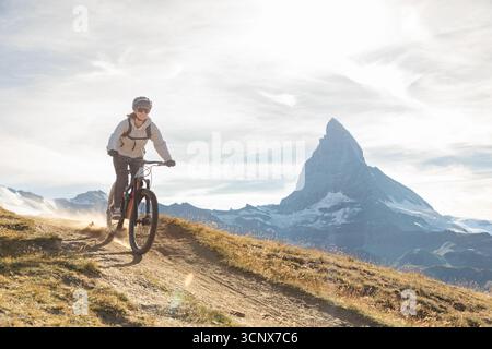 Eine Mountainbikerin fährt auf einem malerischen Weg in den Schweizer Alpen mit dem majestätischen Matterhorn im Hintergrund. Das Bild erfasst Ruhe Stockfoto