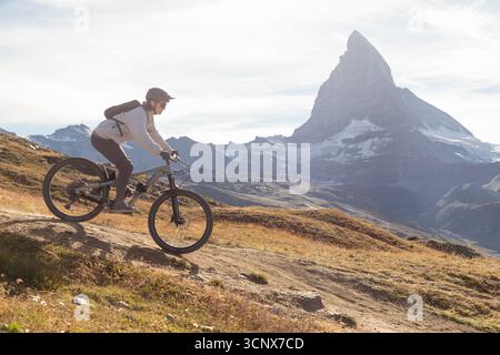 Eine Mountainbikerin fährt auf einem malerischen Weg in den Schweizer Alpen mit dem majestätischen Matterhorn im Hintergrund. Das Bild erfasst Ruhe Stockfoto