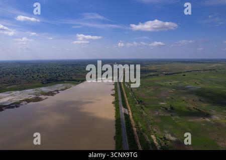 Aus der Vogelperspektive auf einer geraden Straße, die durch die grüne Landschaft führt, wo die Erde auf den Himmel trifft und eine ruhige Reflexion auf das Wasser wirft, Babanruga, Kano, Nigeria. Stockfoto