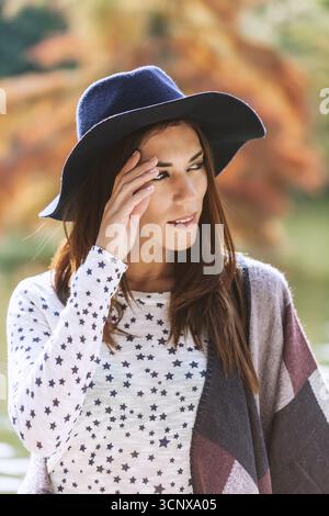 Eine stilvolle Frau mit dunklem, breiter Krempe und einem Top mit Sternenmuster steht im Freien und sonnt sich in der Herbstsonne. Erdtöne des Surroundin Stockfoto
