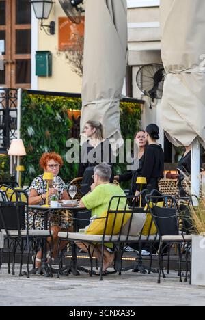 Zwei ältere Damen oder Frauen mittleren Alters sitzen an einem Tisch in einem Restaurant mit einem Kellnerpersonal im Hintergrund. Zwei ältere Freundinnen beim gemeinsamen Abendessen. Stockfoto