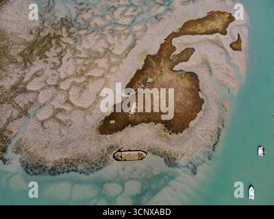 Aus der Vogelperspektive auf die komplizierten Wasserstraßen, die sich durch die schlammige Landschaft ziehen, wo das Land auf das Meer trifft, in der Nähe von Booten, Chiclana de la Frontera, Andalusien, Spanien. Stockfoto