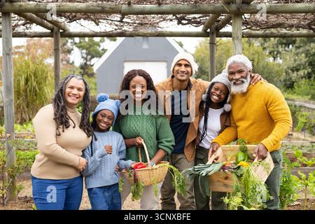 Großfamilie, die unter Pergola im Garten steht und Korb und Kiste mit überlaufendem Gemüse hält Stockfoto