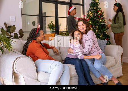 Vielfältige Familie mit Geweih-Haarbändern und weihnachtsmannmütze, die den weihnachtsbaum im Wohnzimmer schmücken Stockfoto