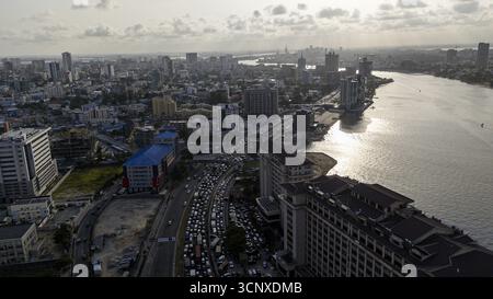 Aus der Vogelperspektive auf das geschäftige Stadtbild, wo die glänzenden Gebäude auf das sonnengeküsste Wasser der Lagune treffen, Lagos, Lagos, Nigeria. Stockfoto