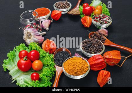 Helle aromatische trockene Gewürze und Gewürze, frisches Gemüse, Holzlöffel zum Kochen auf schwarzem Hintergrund in Form von Rahmen. Bio-Inhaltsstoffe für die Heilung Stockfoto