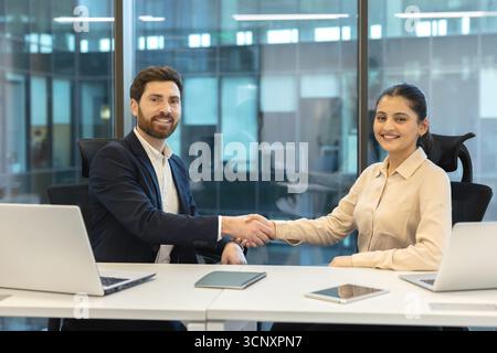 Verschiedene Geschäftsleute schütteln sich die Hände an einem Bürotisch und symbolisieren einen erfolgreichen Abschluss, eine erfolgreiche Partnerschaft und eine erfolgreiche Vereinbarung, die Zusammenarbeit und Teamarbeit in einer Unternehmensumgebung widerspiegelt Stockfoto