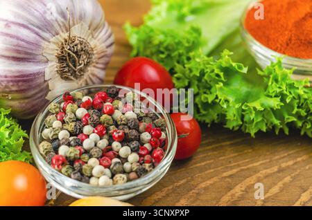 Mischung aus farbigen Paprika in kleiner transparenter Schüssel in Nahaufnahme. Bunte Mischung aus Paprika und Gemüse aus grünem Salat und Kirschtomaten, Knoblauch auf Holz Stockfoto