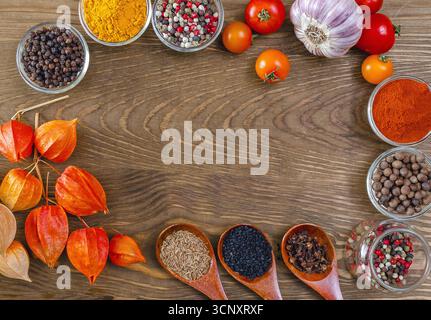 Zusammensetzung der hellen Gewürze von Kurkuma, Paprika, verschiedenen Paprika, Sesam, Kümmel, Zehen und Gemüse einschließlich Kirschtomaten, Knoblauch, Physalis o Stockfoto