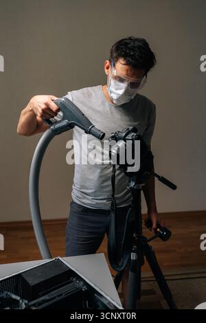 Vertikales Porträt eines professionellen Videografen mit Schutzmaske und Brille zur Desinfektion von Kamera und Computerausrüstung. Stockfoto