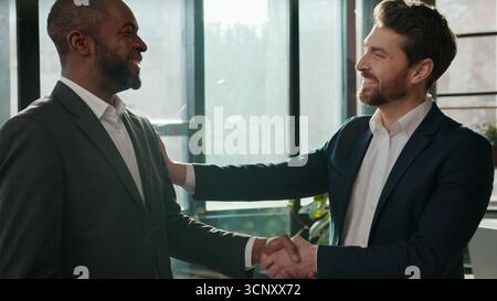 Zwei lächelnde freundliche, vielseitige Geschäftsleute, ein erfolgreiches Handschütteln Männer im Büro Kaukasischer Mann, der die Glückwünsche unterstützt Stockfoto