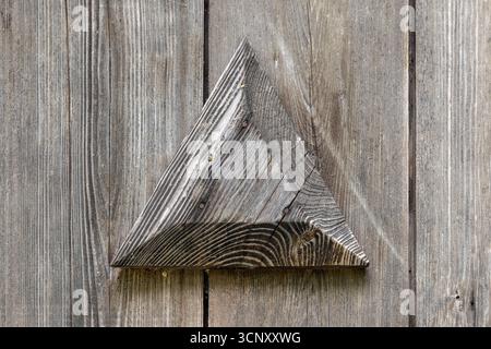 Ein verwittertes Holzdreieck sitzt auf grauen Dielen und zeigt natürliche Körnung und robuste Textur. Ideal für rustikale Einrichtung, Kunsthandwerk, Hintergründe und se Stockfoto