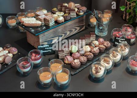 Nachtisch-Buffet-Tisch gefüllt mit verschiedenen Süßigkeiten, einschließlich mehrschichtiger Schokoladenkuchen, farbenfrohen Macarons, Mini-Torten, Cremepuffs und elegantem Glas Stockfoto