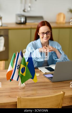 Eine Sprachlehrerin mit leuchtend roten Haaren führt eine Online-Lektion in ihrer Küche durch. Stockfoto