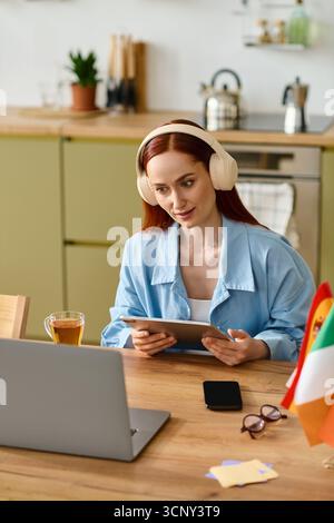 Eine Frau mit rotem Haar führt einen effektiven Online-Sprachkurs von ihrer gemütlichen Küche aus. Stockfoto