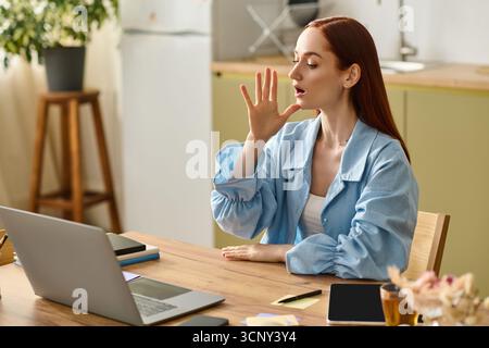 Die rothaarige Lehrerin führt einen interaktiven Online-Sprachkurs mit ihrem Laptop zu Hause durch. Stockfoto