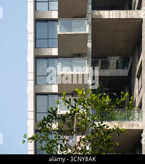 Ein Hochhaus mit moderner Beton- und Glasfassade, mit einer vertikalen Balkonsäule mit Pflanzen. Stockfoto