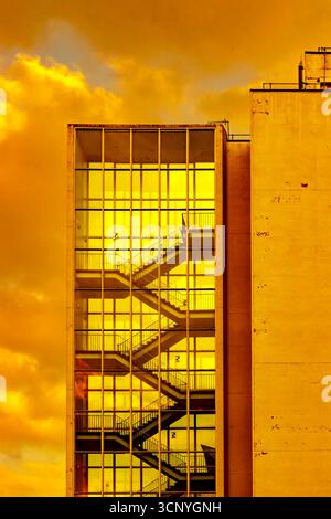 Hochhaustreppe mit Glas und einem markanten orange-gelben Himmel, der während des Sonnenuntergangs auf der Fassade reflektiert, Manchester University UK Stockfoto
