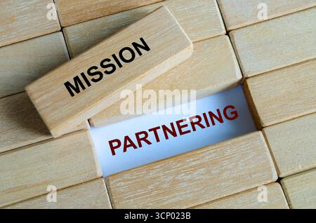 Text der Mission Partnering, geschrieben auf einem blauen Holzblock zwischen anderen auf einer Holzfläche, die die Zusammenarbeit darstellt Stockfoto