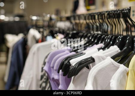 Ein Kleiderständer gefüllt mit ordentlich aufgehängten Hemden in Pastellfarben und neutralen Farben auf schwarzen Kleiderbügeln in einem Geschäft Stockfoto