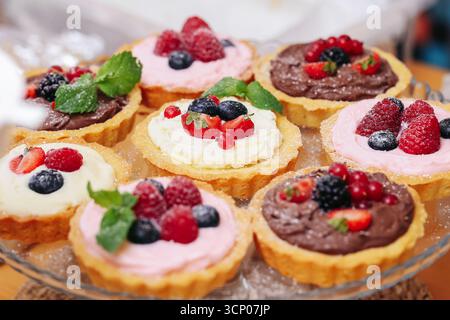 Süße Obsttörtchen mit Sahne und Beeren. Farbenfrohes Dessert mit Erdbeeren Himbeeren Heidelbeeren und Minzblättern. Hausgemachte Konditorei. Stockfoto