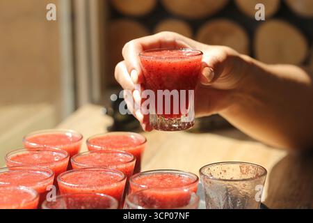 Ein Glas frischer roter Saft in der Hand. Gesunde Frucht Smoothie Nahaufnahme. Erfrischendes Getränk für den Sommer. Natürliches Vitamingetränk. Frisch gepresster Fruchtsaft. Stockfoto