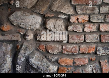Rustikale Mauern aus Ziegeln und Stein mit verstreuten Texturen und Farben. Nahaufnahme einer alten Ziegelsteinmauer mit verschiedenen Texturen Stockfoto
