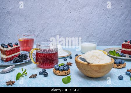 Ein gesundes Frühstücksbild mit Hüttenkäse, einer Schüssel Heidelbeeren, Joghurt und Honig, serviert auf einem Teller vor pastellblauem Hintergrund. Stockfoto