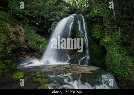 Ein wunderschöner Wasserfall stürzt durch felsiges Gelände, umgeben von lebhaften grünen Pflanzen und Bäumen in einer ruhigen Umgebung. Stockfoto