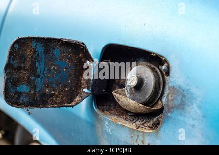Die offene Klappe des alten, verlassenen Autos und die geschlossene Tanköffnung. Nahaufnahme, blaues Auto, keine Leute Stockfoto