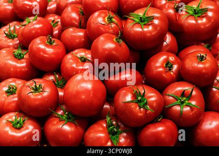 Nahaufnahme selektiver Fokus: Schöne runde, reife, frische rote Tomaten, die auf dem lokalen Markt zum Verkauf angeboten werden, unter anderem farbenfrohen Gemüsesorten. Stockfoto