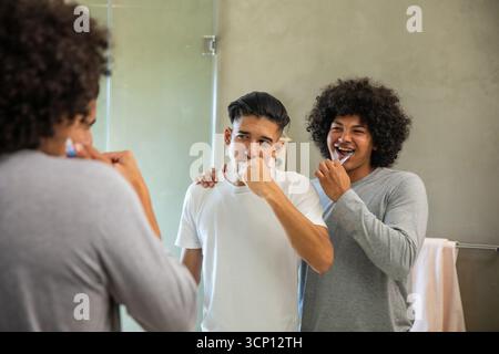 Männliche Mitbewohner putzten die Zähne am Waschbecken im Bad mit Zahnbürsten und Handtuchhalter neben dem Spiegel Stockfoto