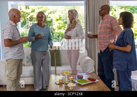 Freunde, die um einen hölzernen Couchtisch stehen und sich im Wohnzimmer unterhalten und Weingläser halten Stockfoto