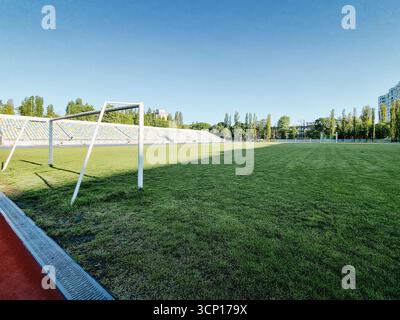 Empty football field in the morning. Shadow covering half of the field, big goal gate close to the camera. Stockfoto