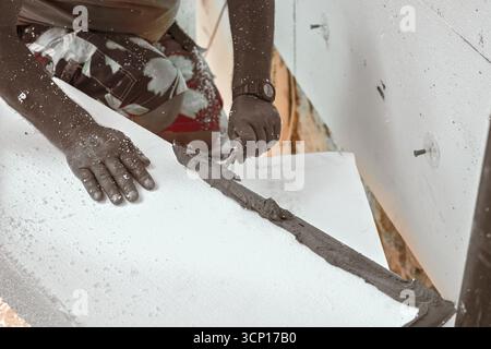 Installation der weißen Polystyrol-Wärmedämmung, Detail auf Arbeiter Hand legen grauen Kleber Zement auf weißen Brettern Stockfoto