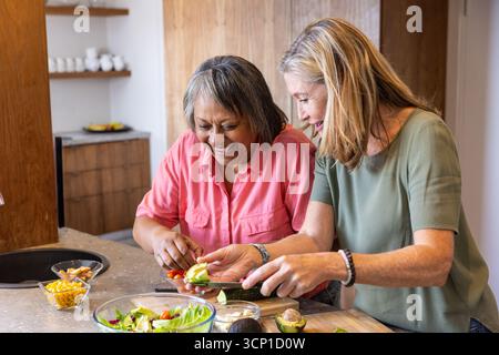 Verschiedene Freunde bereiten Salat auf der Kücheninsel mit Avocado und Kirschtomaten zu Stockfoto