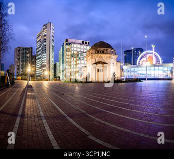 Eine lebhafte Nachtszene am Centenary Square, Birmingham, mit einem Kuppeldenkmal, modernen Glasfassaden und einem hell beleuchteten Riesenrad – Captu Stockfoto